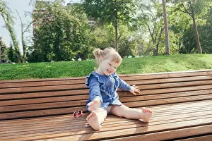 Little girl sitting on the bench and laughing in a city park on a warm sunny day