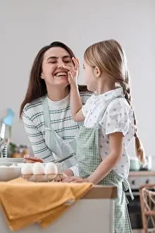 Little girl touching her mother's nose while cooking in kitchen on Easter day