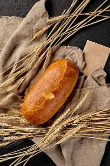 Burlap Prints: Loaf of freshly baked bread on cut of burlap with ears of wheat on black background