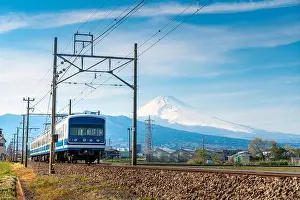 A local train of JR Izuhakone Tetsudo-Sunzu Line traveling through the countryside on a sunny winter day and Mt. Fuji in Mishima, Shizuoka, Japan