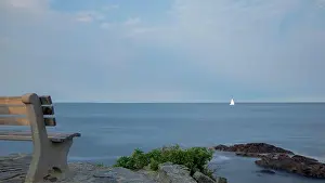 Contemplative Prints: Lone empty bench, facing distant sailboat on smooth ocean