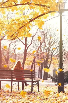 Desperation Prints: Lonely woman sitting on bench at city park. Beautiful autumn foliage background