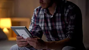 Bedding Prints: Lonely young man sitting on bed, holding family photo, missing wife, sadness