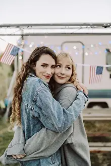 Fourth Prints: Lovely shot of two Spanish females hugging each other on background of the US flags