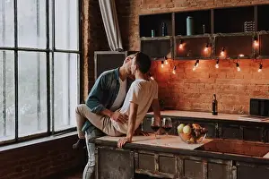 Cuddling Prints: Loving gay couple at home. Two handsome passionate men hugging and kissing on kitchen