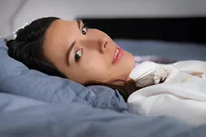 Awake Prints: Low angle closeup view of a refreshed young woman resting in bed lying back on her pillow turning her head to look