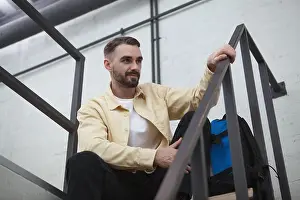 Restful Prints: Low angle shot of a handsome bearded male tourist with a backpack sitting on the staircase at hotel room