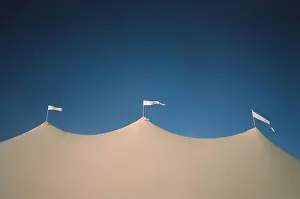 A low angle shot of three white flags waving in the wind on top of a medieval-style tent under a blue sky