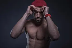 Threat Prints: Low key image of a fit shirtless young man wearing a red beanie hat in a black background