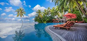 Luxurious beach resort with swimming pool seaside beach chairs or loungers under umbrellas with palm trees and blue sky. Summer travel hotel vacation
