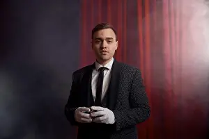 Velvet Prints: Magician wearing suit standing with cane on stage decorated red velvet curtain