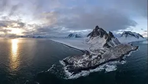 Majestic aerial view of a snow-covered mountainous peninsula in Iceland during sunset with glimmering sea