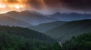 Majestic drone view of bright sun setting on cloudy evening sky over green hilly terrain