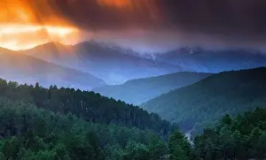 Majestic drone view of bright sun setting on cloudy evening sky over green hilly terrain