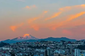 The majestic snowcapped Andes peak of the Cayambe volcano illuminated at sunset with the cityscape of Quito, Ecuador
