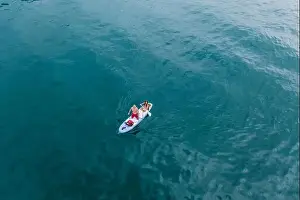 Lake Garda Prints: Malcesine, Italy - August 7, 2019: Aerial drone shot view of a man and young girl on surfboard in lake garda