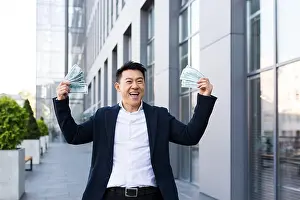 Optimistic Prints: Male asian businessman rejoices holding a lot of cash dollars got a big win and payout