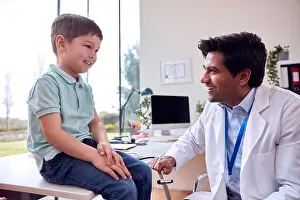 White Coat Prints: Male Doctor Or GP Wearing White Coat Examining Smiling Boy Testing Reflexes