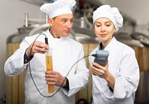 Producing Prints: Male and female brewers measuring pH in beer with digital meter
