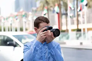 Vacationer Prints: A male photographer paparazi in a blue shirt is watching an object taking photos