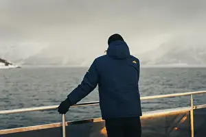 Brim Prints: Man in blue coat on boat looking at misty arctic mountains in the Lyngen Alps