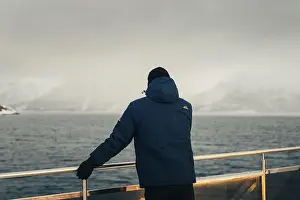 Brim Prints: Man in blue coat stood on tour boat looking at misty Lyngen Alps in Norway