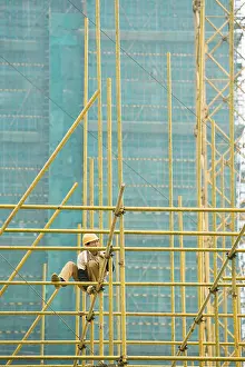 Asians Prints: Man in hard hat perched on scaffolding, building in background
