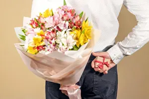 Valentines Prints: A man holds a gift with a red bow in his hands and hides it behind his back with a bouquet of flowers