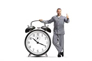 Awake Prints: Man in pajamas leaning on a big alarm clock and gesturing thumbs up isolated on white background