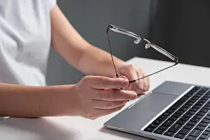 Eyesight Prints: Man plays nervously with eyeglasses working at laptop