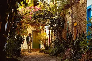 Moment Prints: A man plays a saxophone in a narrow street with vibrant plants and flowers on both sides
