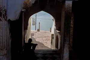 Archway Prints: Man sitting in an archway looking into the ghats of Pushkar, Rajaasthan, India