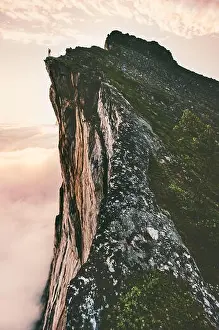 Man standing on cliff edge mountain ridge above sunset clouds travel adventure lifestyle summer journey vacations