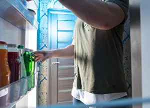 Engrossed Prints: Man standing in the open door of a refrigerator selecting a beverage form bottles on the shelf viewed from inside