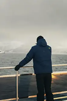 Man stood on edge of arctic tour boat looking at Lyngen Alps in winter in Norway