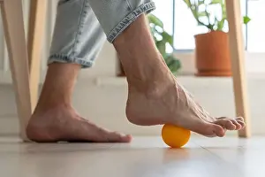 Fatigue Prints: Man using silicone ball for foot massage during long sedentary work, legs close-up