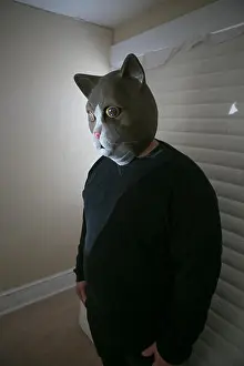 Mattress Prints: man wearing a mask of a cat standing in a bed room in front of a mattress leaning against a window
