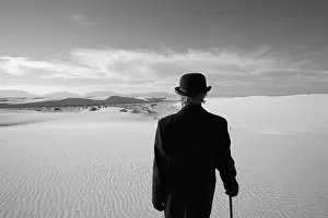 Contemplative Prints: man wearing overcoat and bowler hat looking out at white sand dune desert