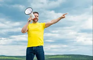 Megaphone Prints: man in yellow shirt shout in megaphone on sky background. point finger