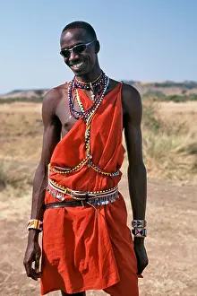 Maasai Prints: A Masai man in traditional outfit poses wearing sunglasses in the Masai Mara in Kenya