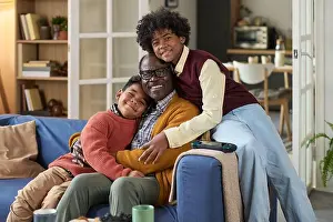 Sibling Prints: Mature Black Man Hugging Two Black Boys Smiling on Living Room Sofa
