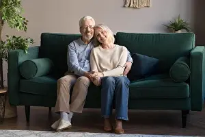 Pensioners Prints: Mature couple embracing sitting on couch posing for camera