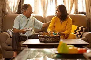 Remote Control Prints: Mature couple playing video game sitting together on sofa in living room