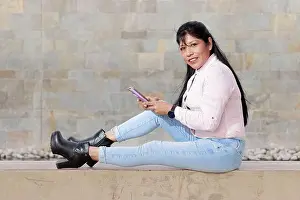 Latina Prints: Mature latina woman interacting with her mobile, striped shirt on worn jeans