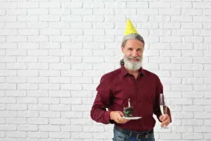 Confection Prints: Mature man with piece of birthday cake and glass of champagne on brick wall background