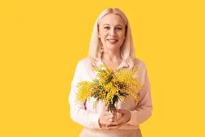 Mimosa Prints: Mature woman with mimosa flowers on yellow background. International Women's Day
