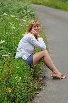 Contented Prints: Mature woman wearing a white shirt and short skirt sitting on the roadside