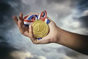 Reward Prints: Medal for first place in the athlete palm against a dramatic sky