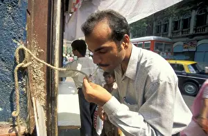 Cigarettes Prints: a Men take fire for his cigarettes on a rope line fire station at a road in the city centre of Mumbai in India