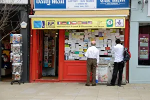 Searching Prints: Two men looking at advertisements in a newsagent shop window, London, England, UK